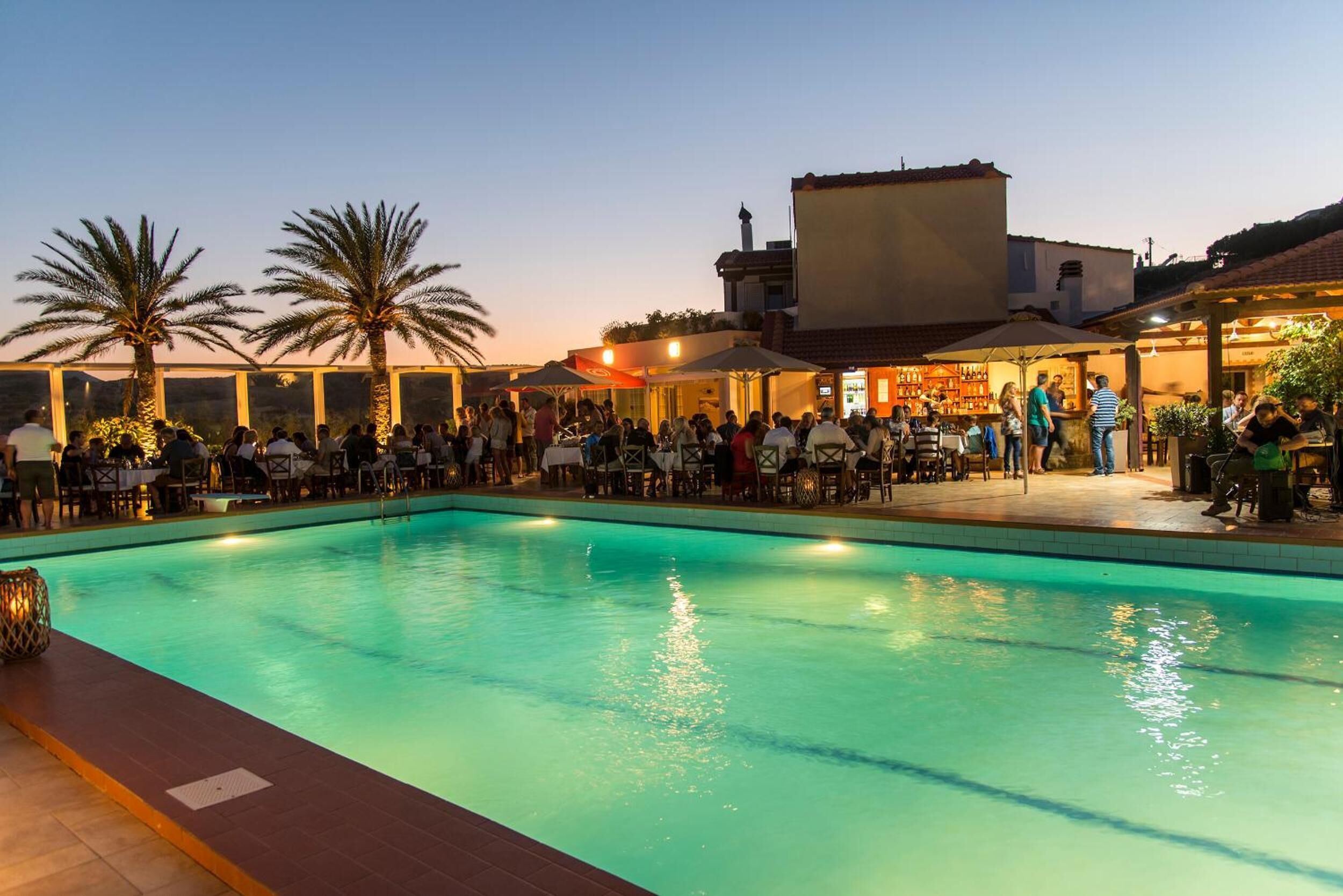A poolside area with a bar and outdoor seating, surrounded by palm trees and buildings.