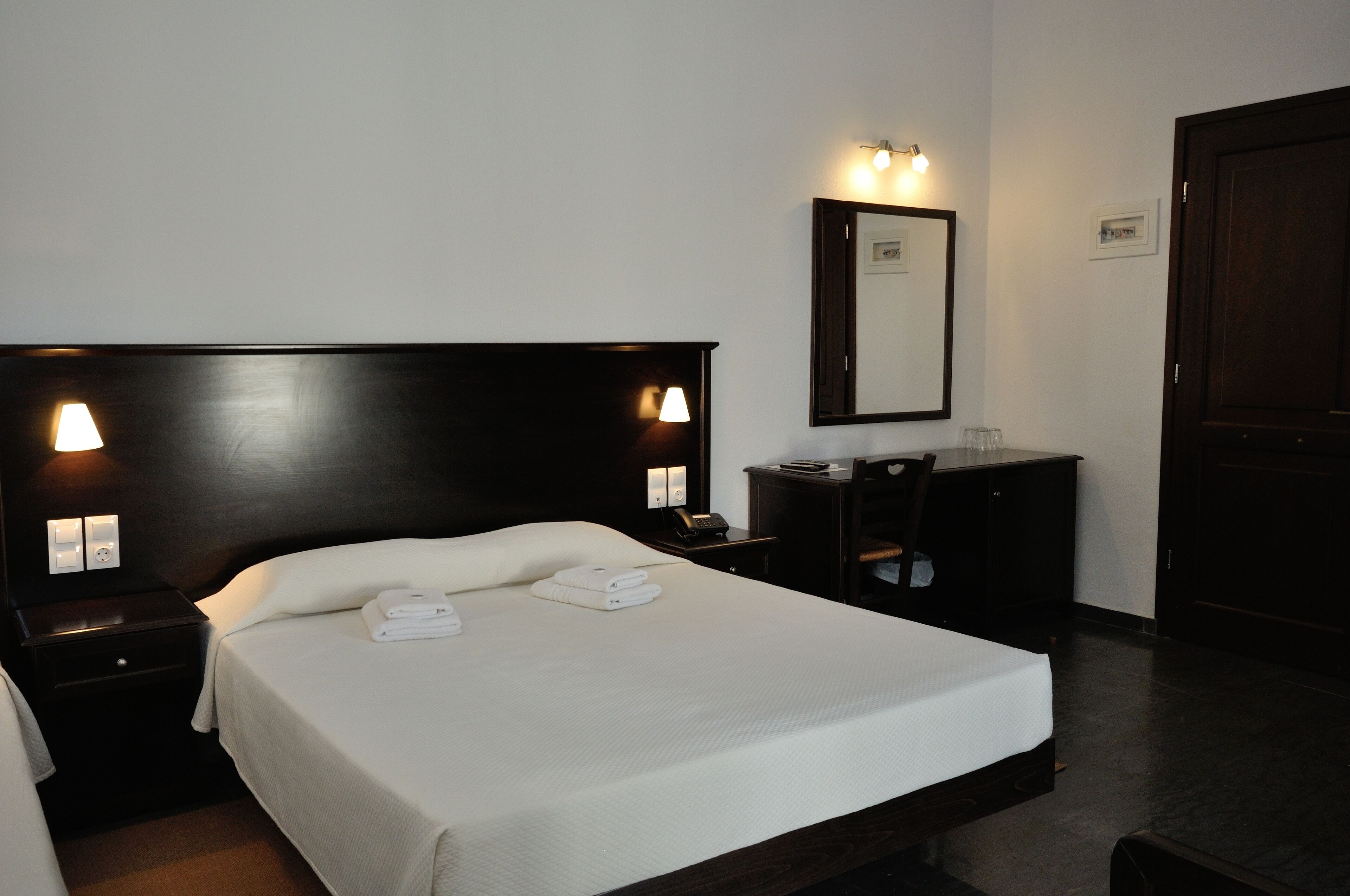 A hotel room with a large bed, two bedside tables, a desk, and a wardrobe.