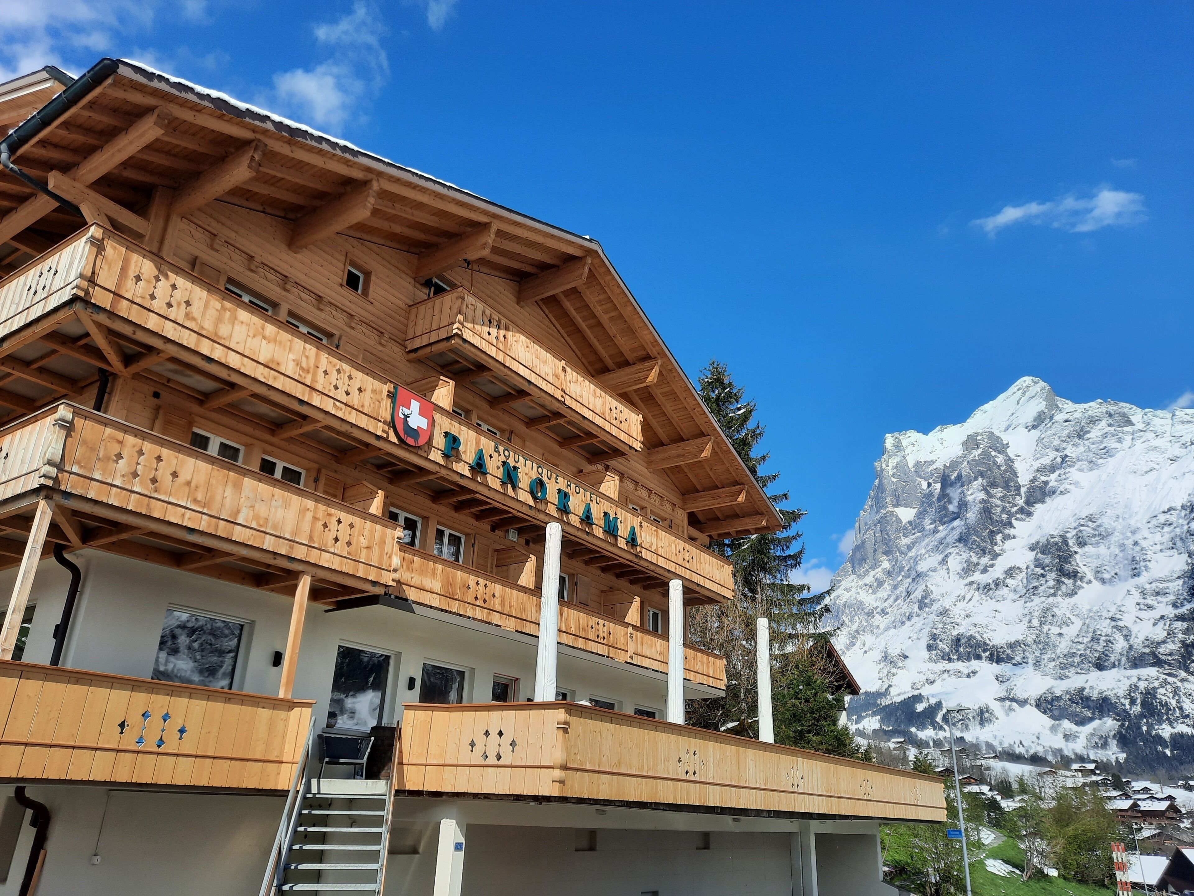 Un edificio de madera de varios pisos con balcones, un emblema de la bandera suiza y montañas al fondo.