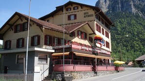 A hotel with a restaurant on the ground floor, a mountain backdrop, and a street lamp in the foreground. - Hotel & Restaurant Alpenrose (Innertkirchen)
