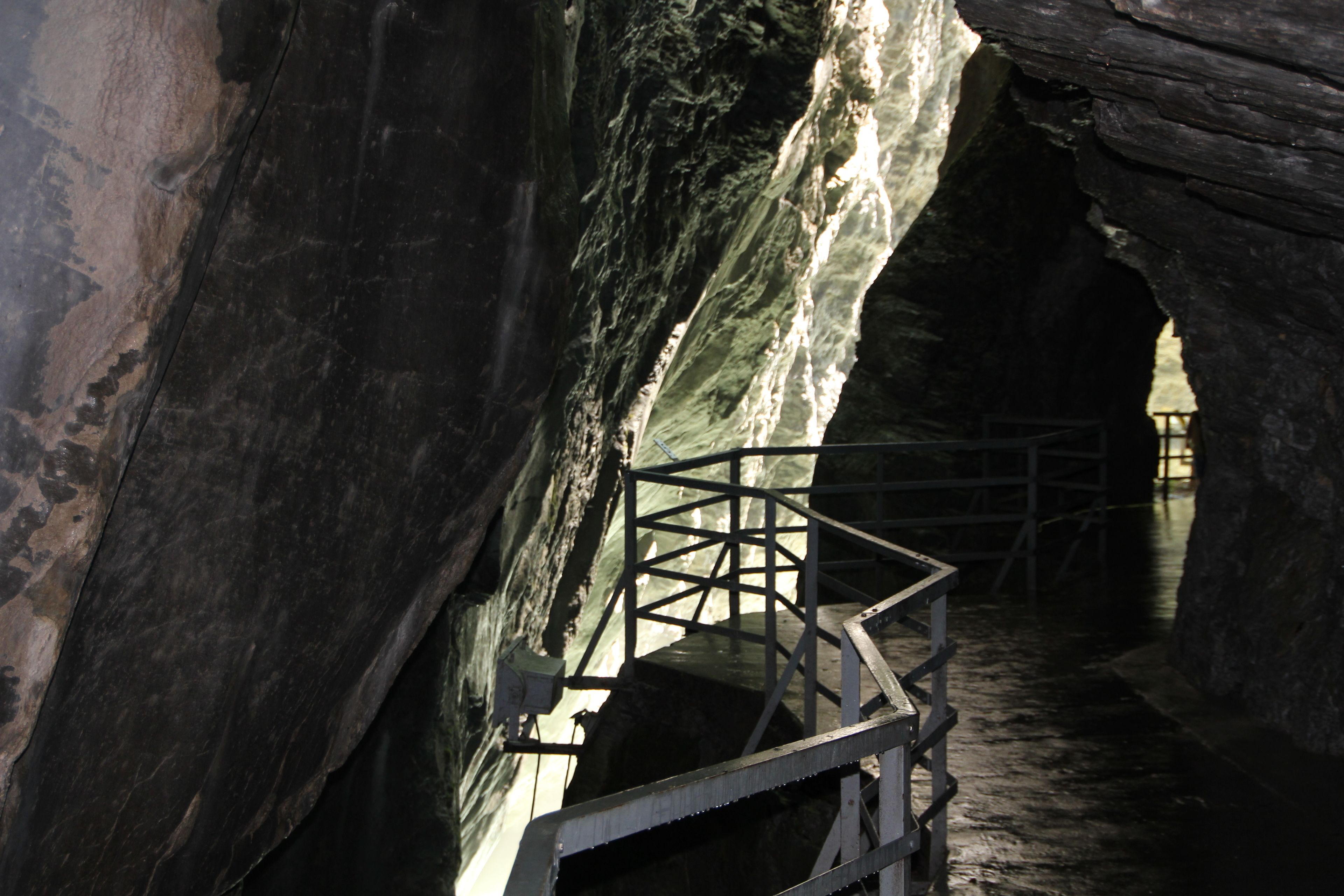 Ein schmaler Durchgang mit einer Metalltreppe, die an einer felsigen Wand hinauf führt.