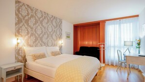 A bedroom with a bed, bedside table, and a desk with a chair. - Hôtel du Grand-Pré (Marly)