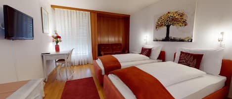 Habitación de hotel con dos camas, un escritorio, un televisor y una ventana con cortinas.
