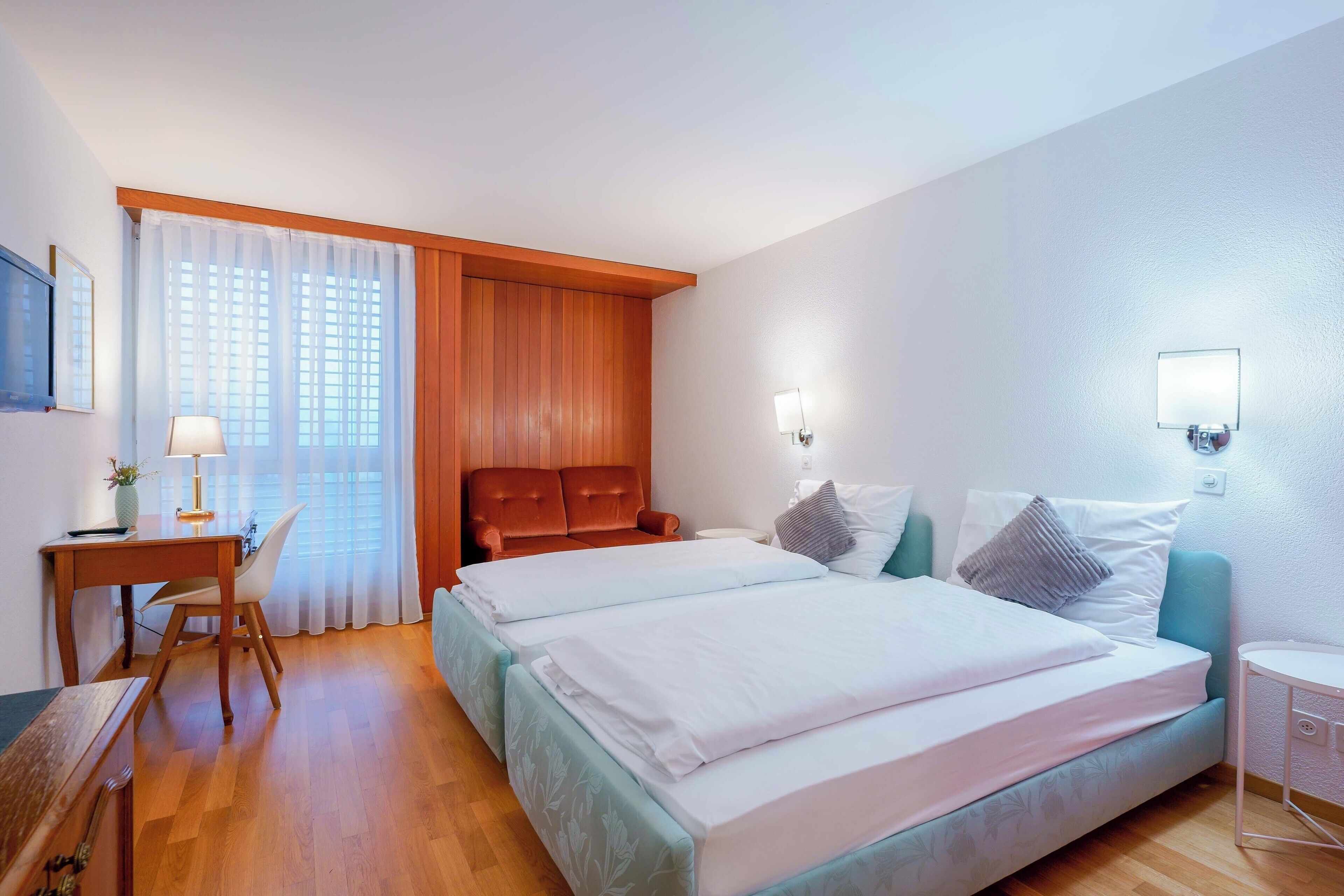 A hotel room with a bed, a desk, a chair, and a window with curtains.