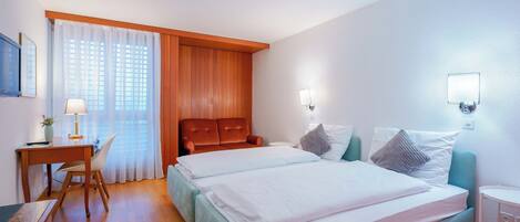 A hotel room with a bed, a desk, a chair, and a window with curtains.