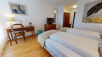 Une chambre d’hôtel avec un bureau en bois, une chaise, une télévision, un lit avec une literie blanche et un tableau au mur.