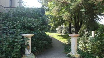 A paved pathway flanked by lush greenery and two classical-style columns.