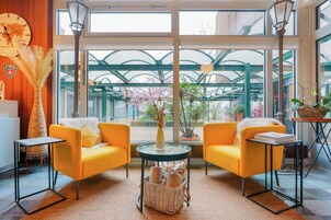 Una habitación luminosa con sofás amarillos, una mesa de vidrio y vistas a una construcción verde en el exterior.