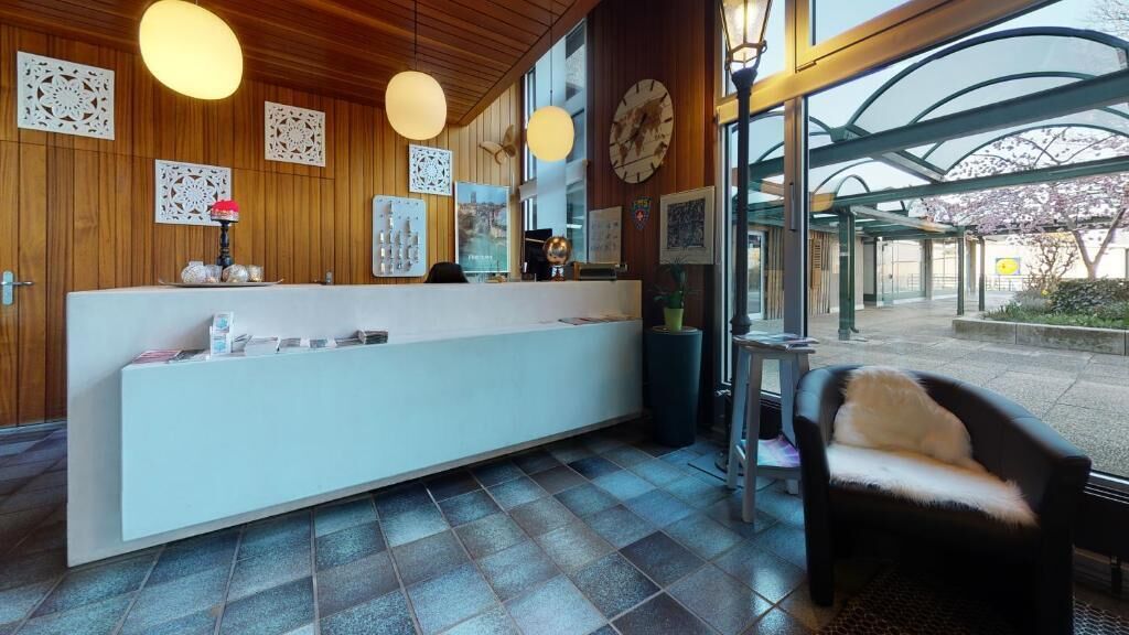Een receptie met een houten balie, een wachtruimte met een stoel en uitzicht buiten door grote ramen.