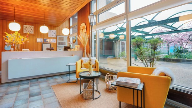 A modern reception area with a wooden ceiling, large windows, and a reception desk. - Hôtel du Grand-Pré (Marly)
