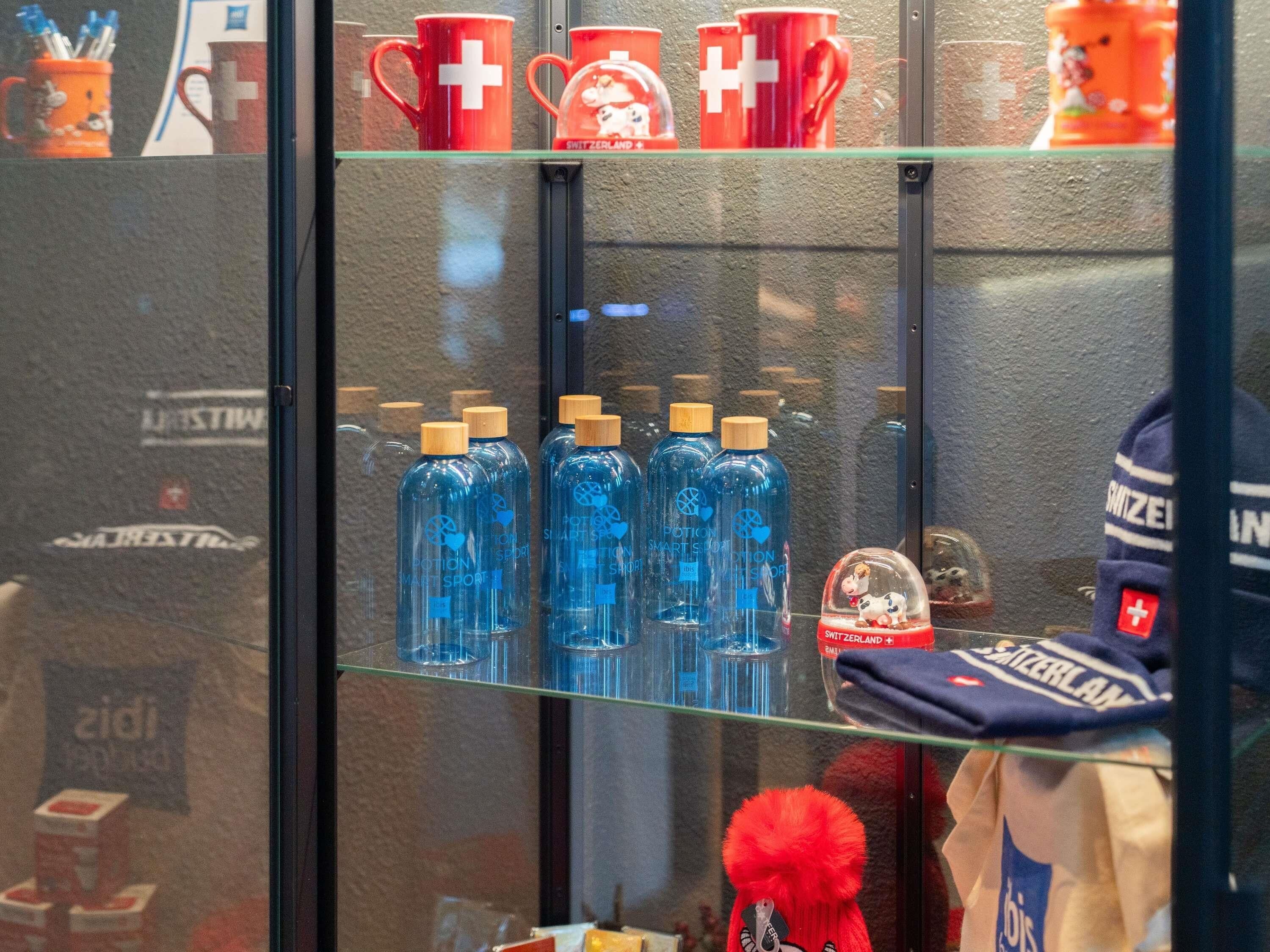 Una exposición de tazas rojas con una cruz blanca, botellas azules con tapones de madera y un peluche rojo.