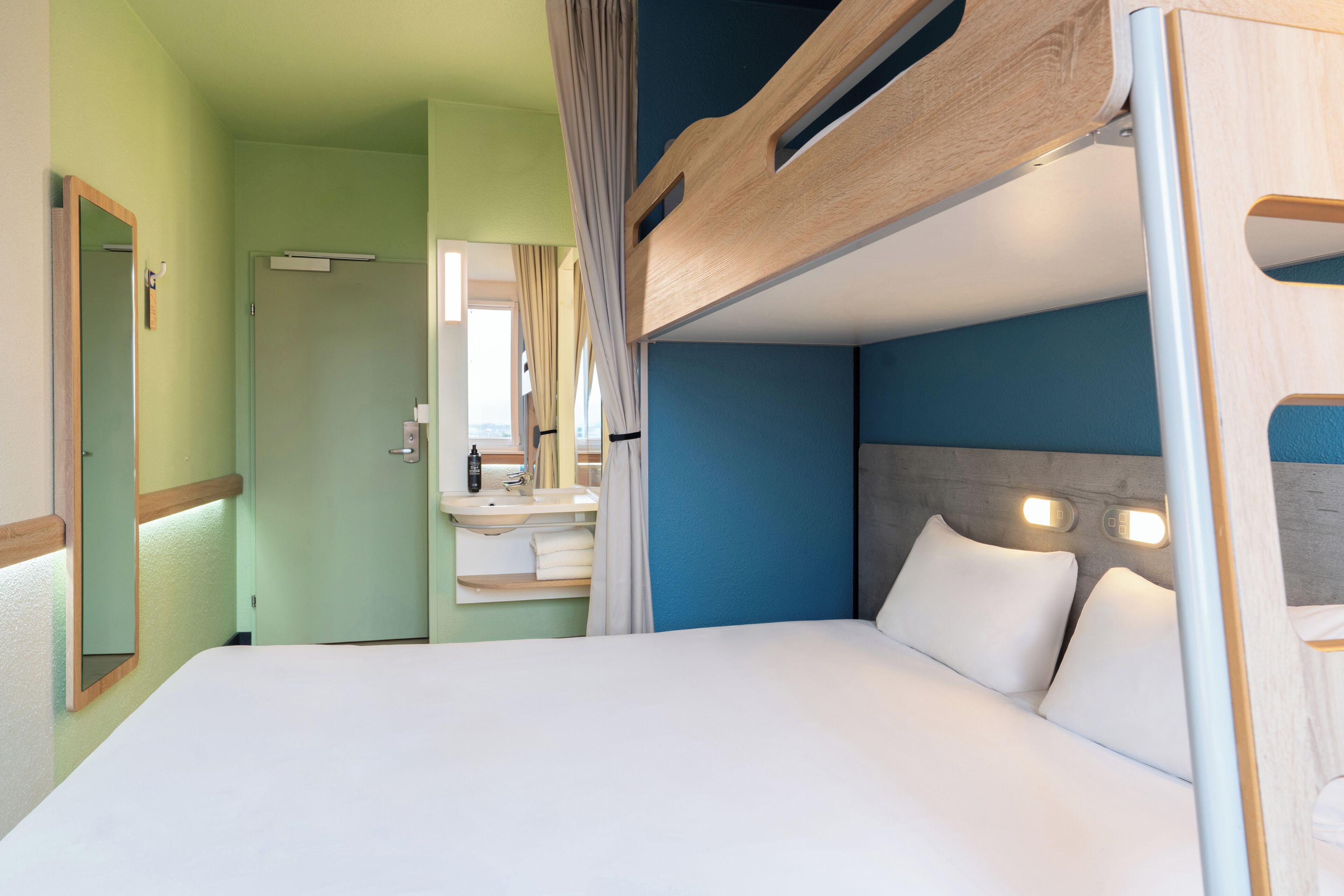 A bunk bed with a headboard, a bedside table with a mirror, and a window with curtains.