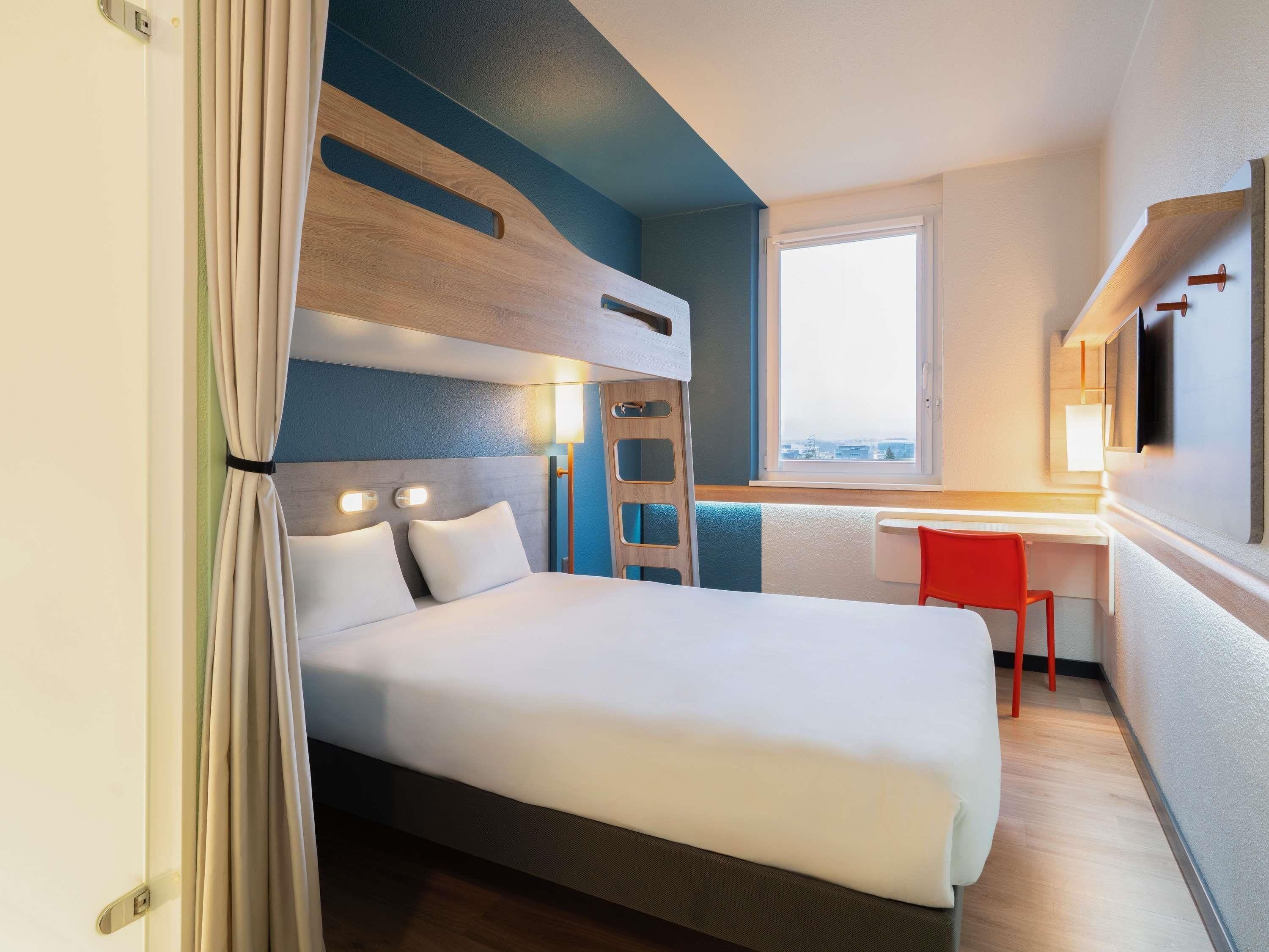 Une chambre d’hôtel avec un lit superposé, un bureau, une chaise, une fenêtre et une vue sur la ville.