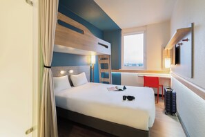 A hotel room with a bed, a desk, a chair, a suitcase, and a window. - ibis budget Geneve Aeroport (Vernier)