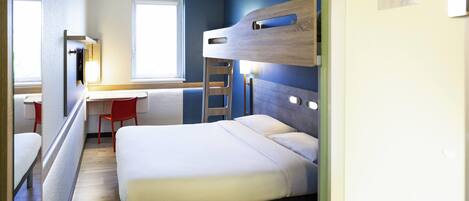 Una habitación de hotel pequeña con una cama litera, un escritorio y una silla, además de un ventanal.