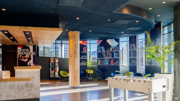 A modern lobby with a reception desk, a foosball table, and a bookshelf with books. - ibis budget Geneve Aeroport (Vernier)