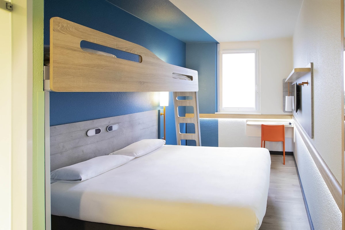 Quarto com cama de solteiro e beliche, escrivaninha, cadeira e televisão.