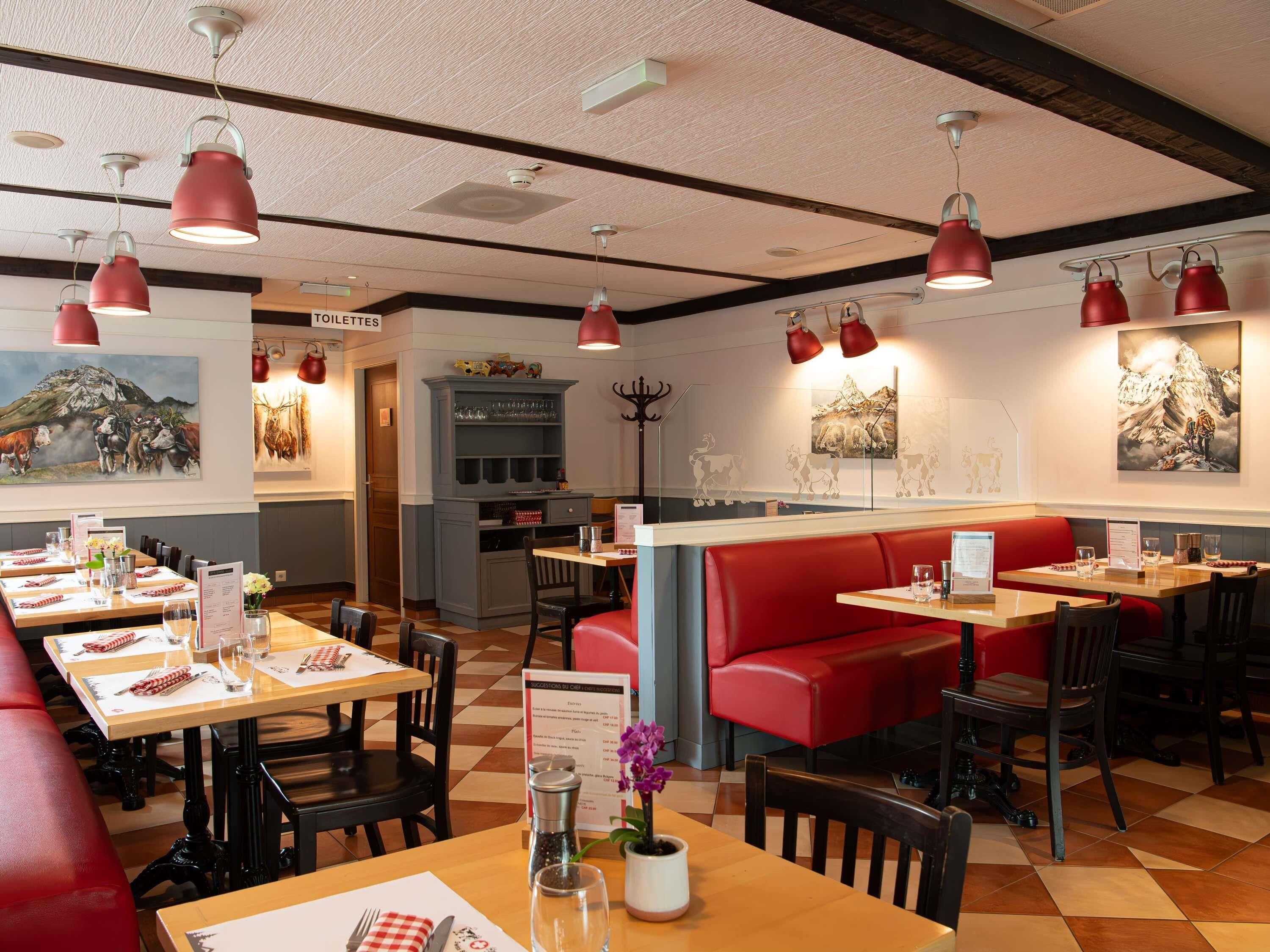 A restaurant with red booths, wooden tables, and pendant lighting.