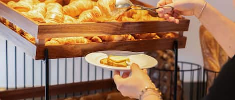Una persona sirviéndose croissants de un expositor de madera.