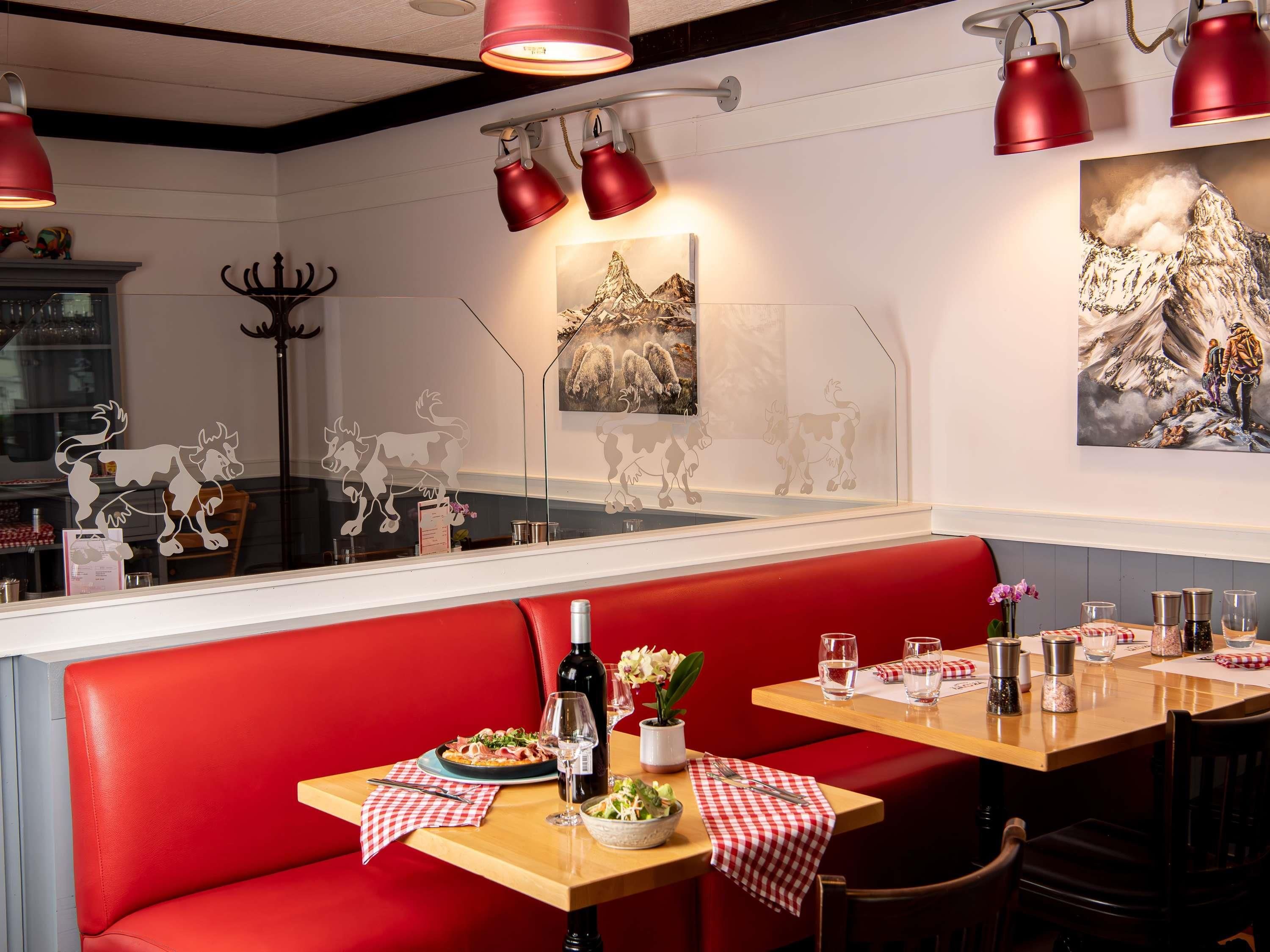 Interior de restaurant amb seients vermells, taula de fusta i obra d'art a les parets.