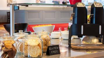 Un comptoir de buffet proposant des options sans gluten, une machine à café et divers aliments présentés dans des récipients en verre.