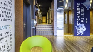 A modern hotel lobby with a staircase, a green chair, and a sign reading "PLANET 21". - ibis budget Geneve Aeroport (Vernier)