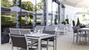 An outdoor dining area with tables and chairs, large windows, and umbrellas. - ibis budget Geneve Aeroport (Vernier)