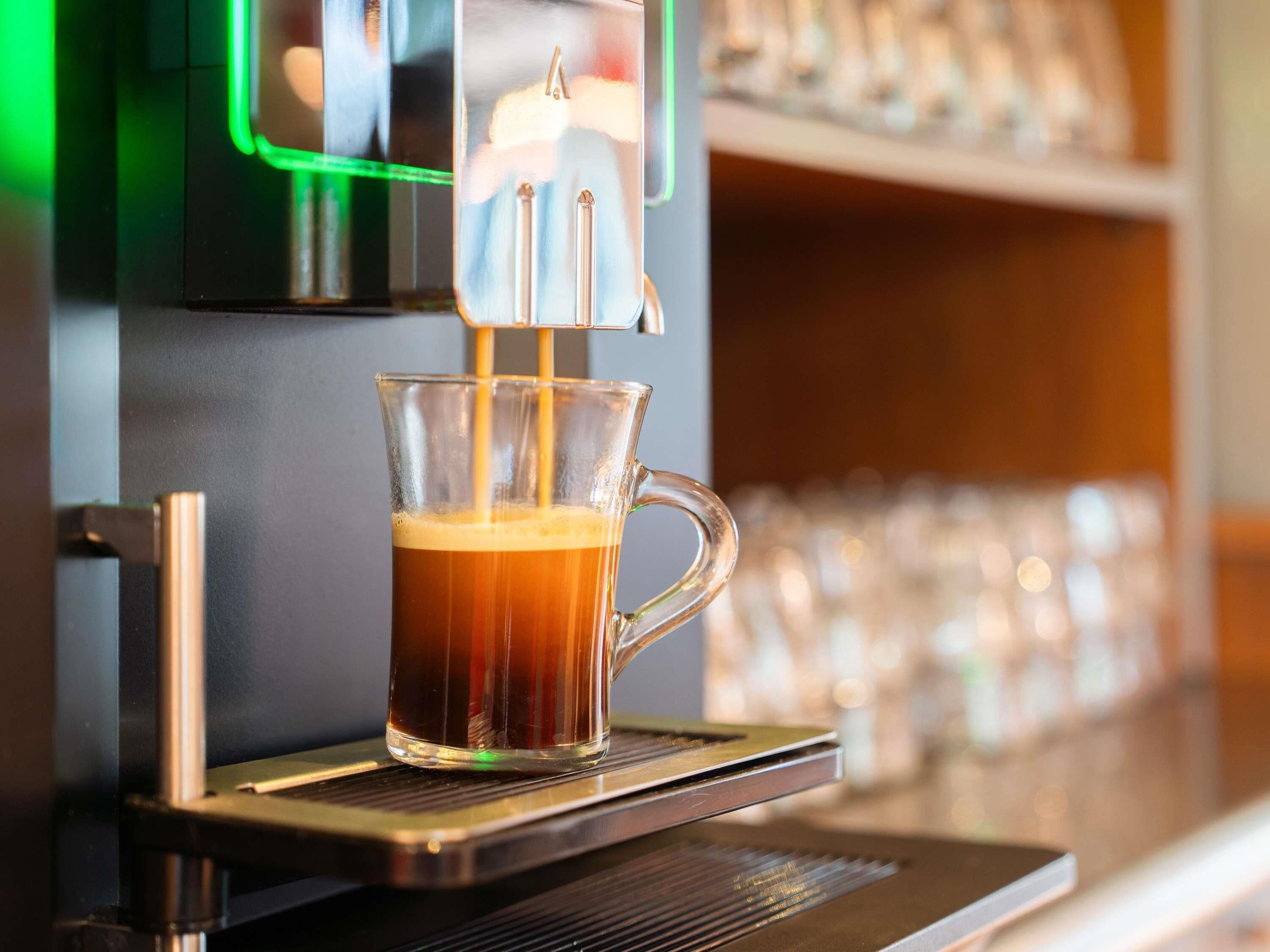 A coffee machine dispensing coffee into a clear glass cup.