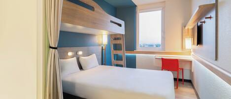 A hotel room with a bed, a desk, a chair, a window, and a TV mounted on the wall.