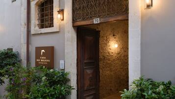 A building entrance with a wooden door, a number '70' sign, and potted plants.