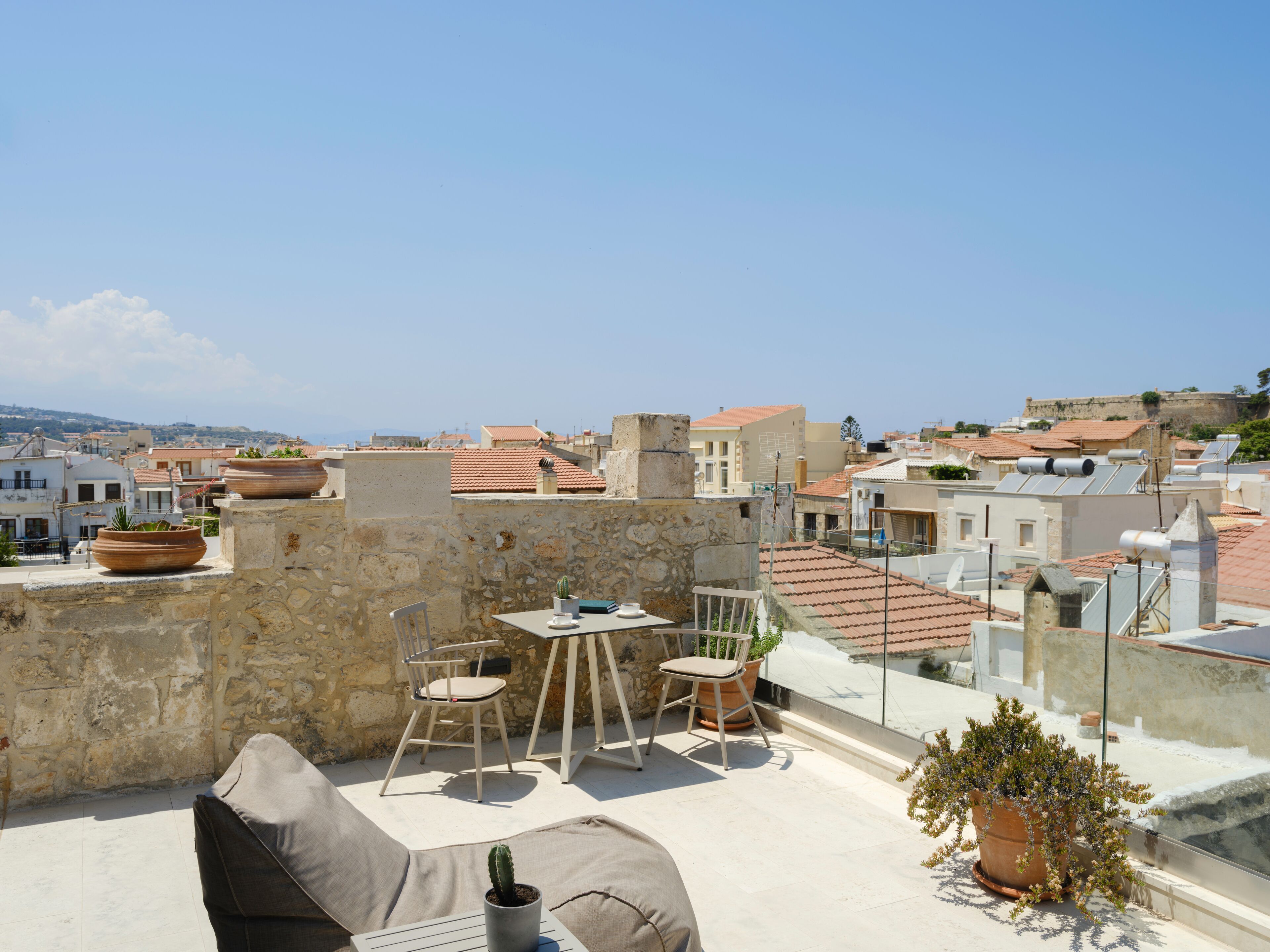 A rooftop terrace with a table and chairs, potted plants, and a view of the cityscape.