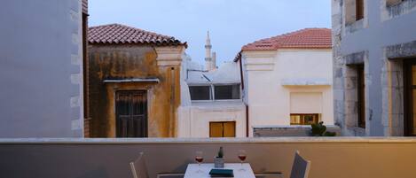 A balcony with a table and chairs, overlooking a street with buildings.