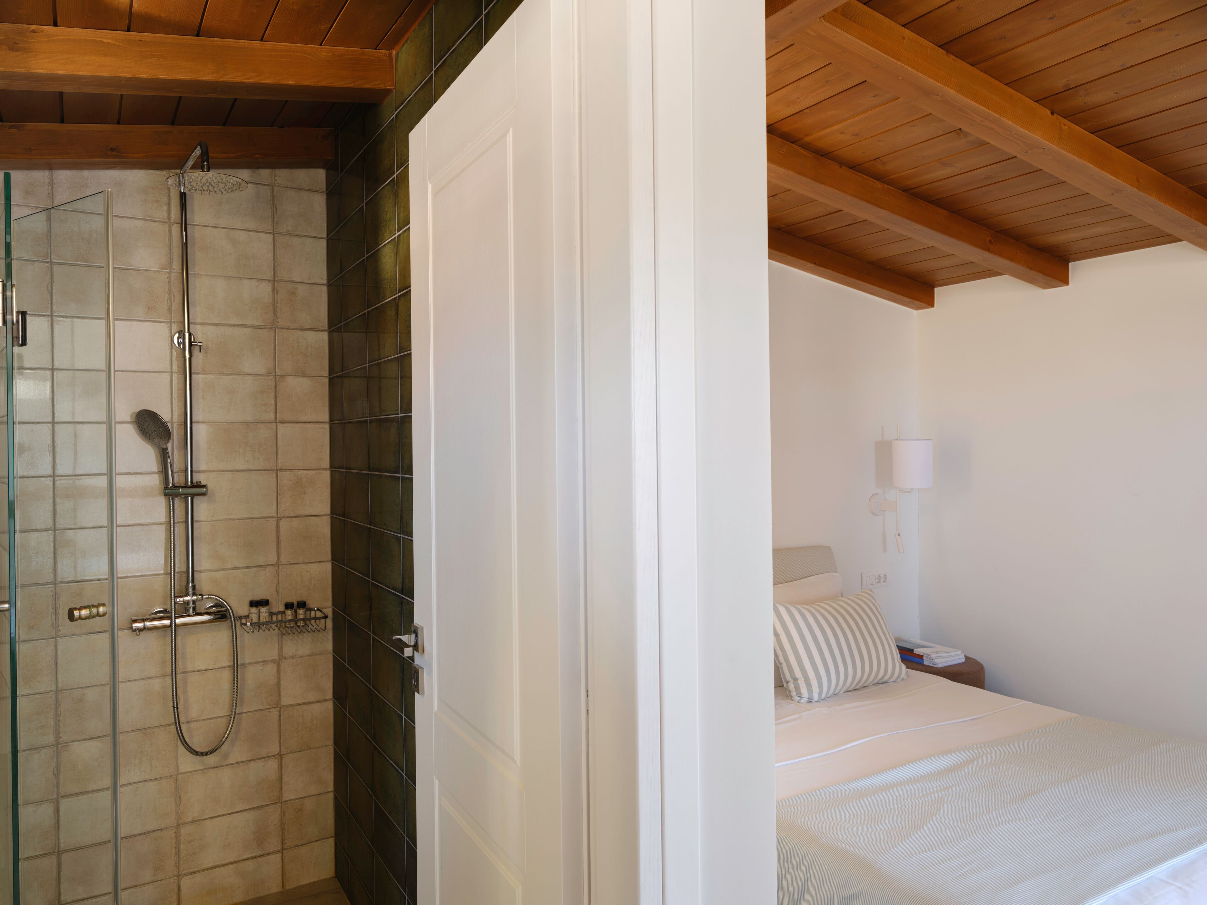 Un dormitorio con cama, mesita de noche, lámpara y techo de madera.