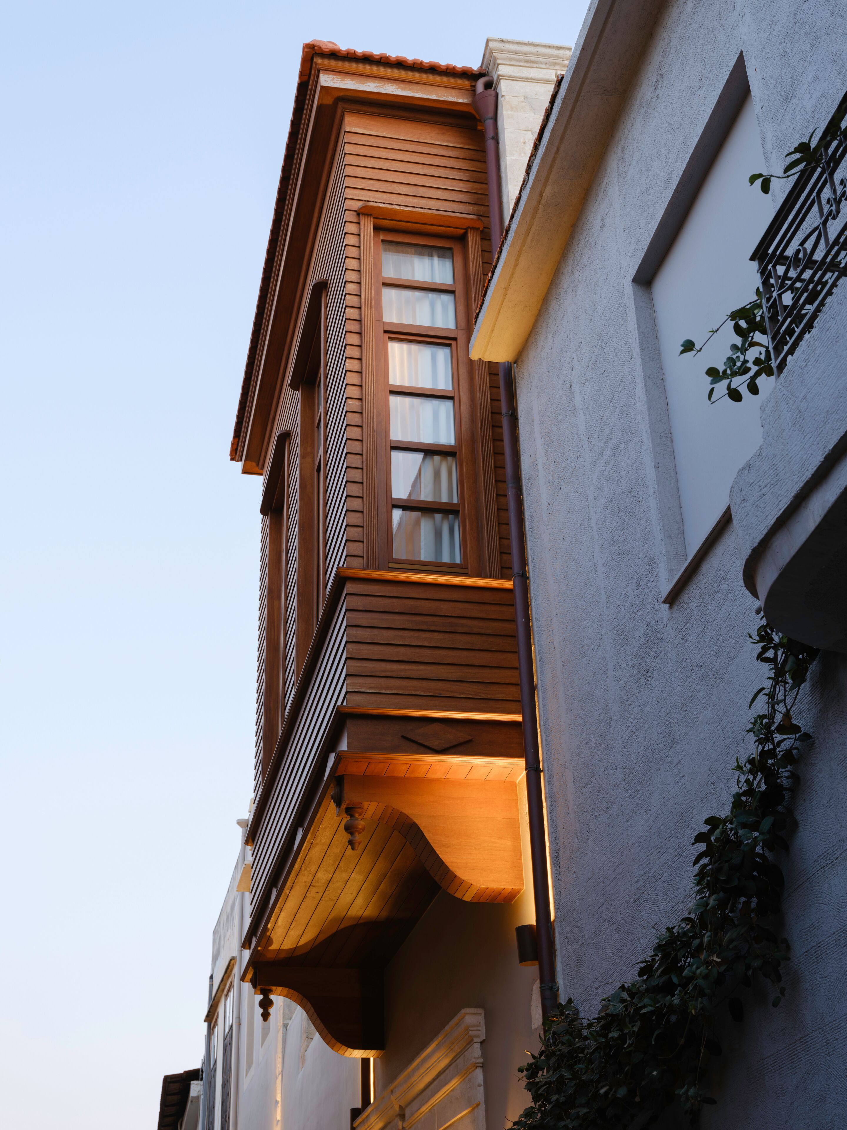 Ein Gebäude mit einem Holzbalkon, einem fensterartigen Öffnung mit Vorhängen und einer Pflanze auf der rechten Seite.