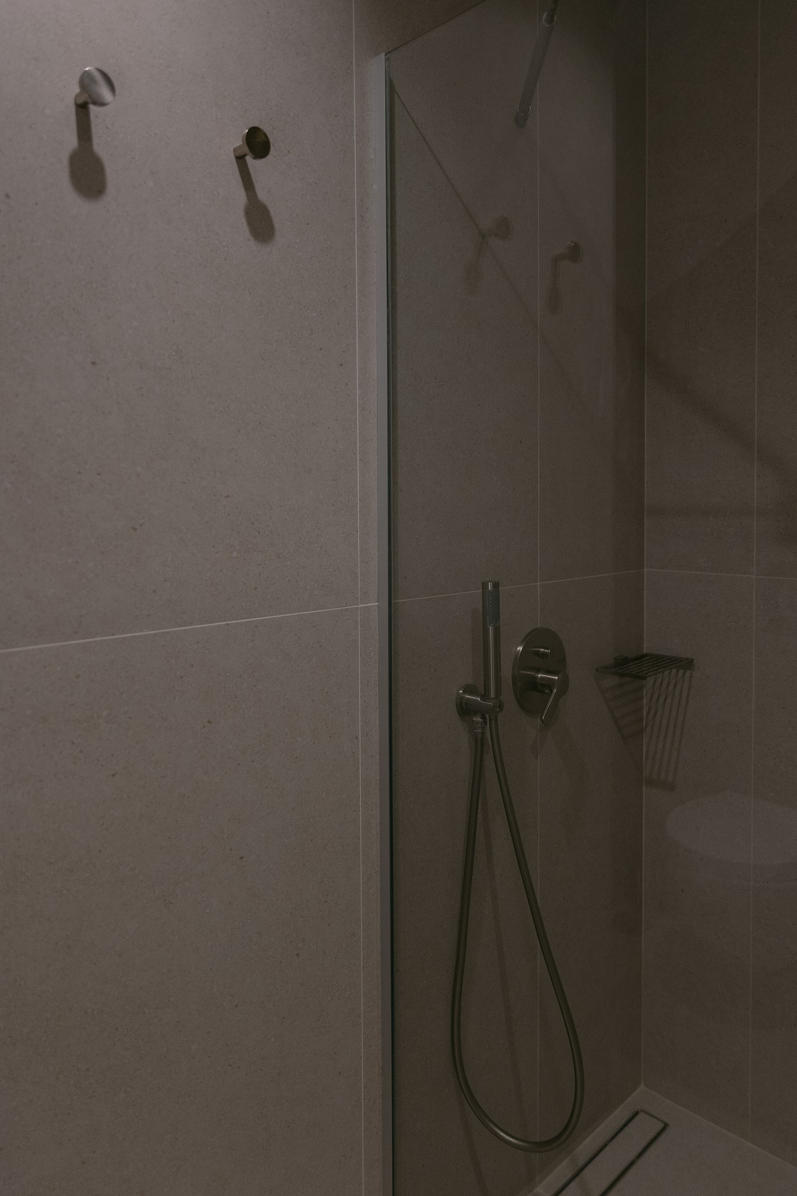 Ducha con cerramiento de vidrio, cabezal de ducha de mano y grifo empotrado.
