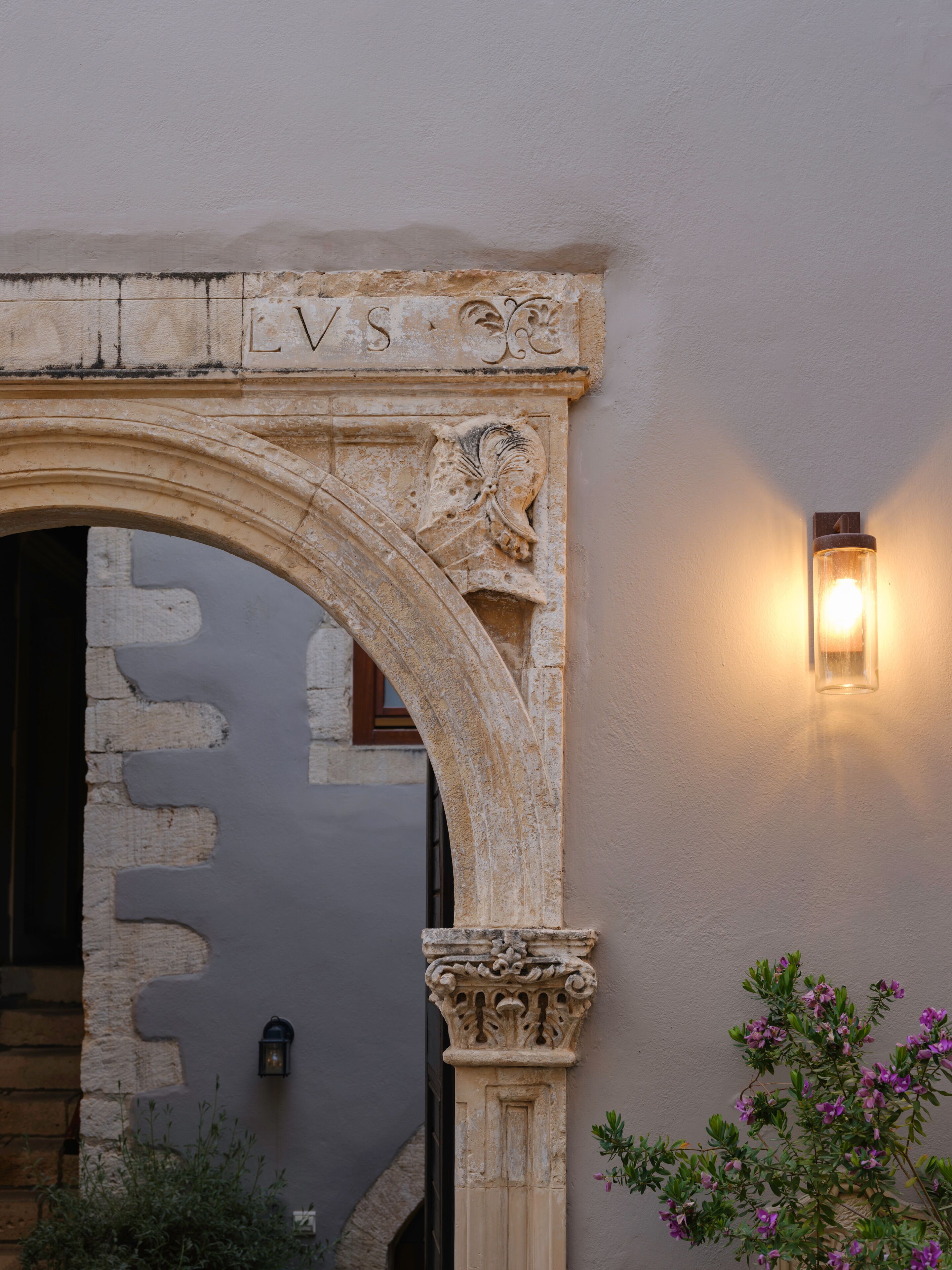 Un arco de piedra con inscripciones talladas y un accesorio de luz fijado a la pared.