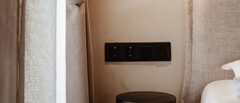 A hotel room with a bed, a bedside table, a wall-mounted light fixture, and a curtain.