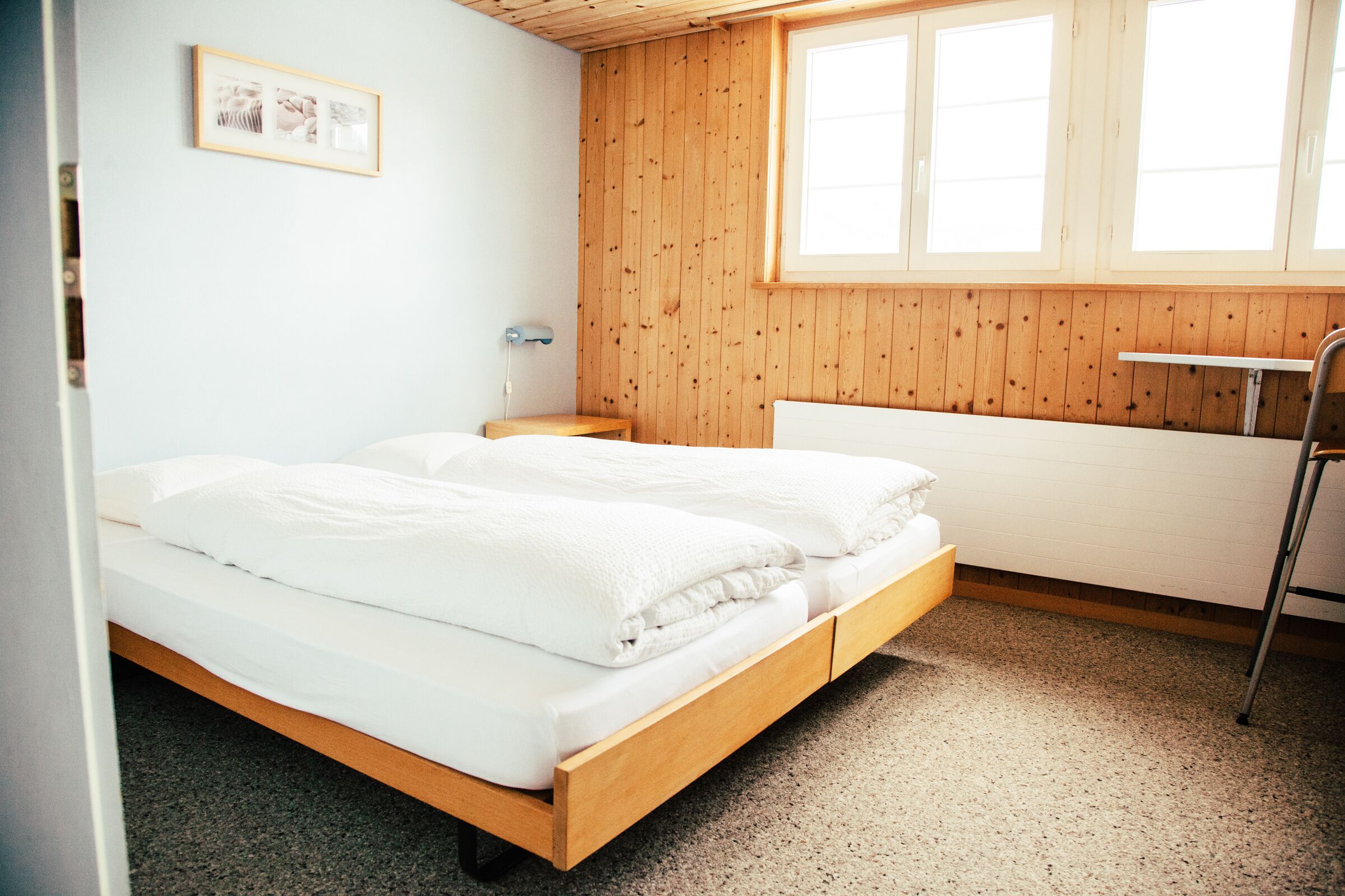 A bedroom with a wooden bed, a small bedside table, a radiator, and a window with blinds.