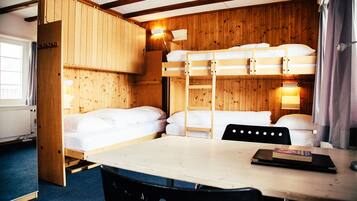 Une chambre avec un lit superposé, une table et des chaises, des murs en bois et une fenêtre avec des rideaux.