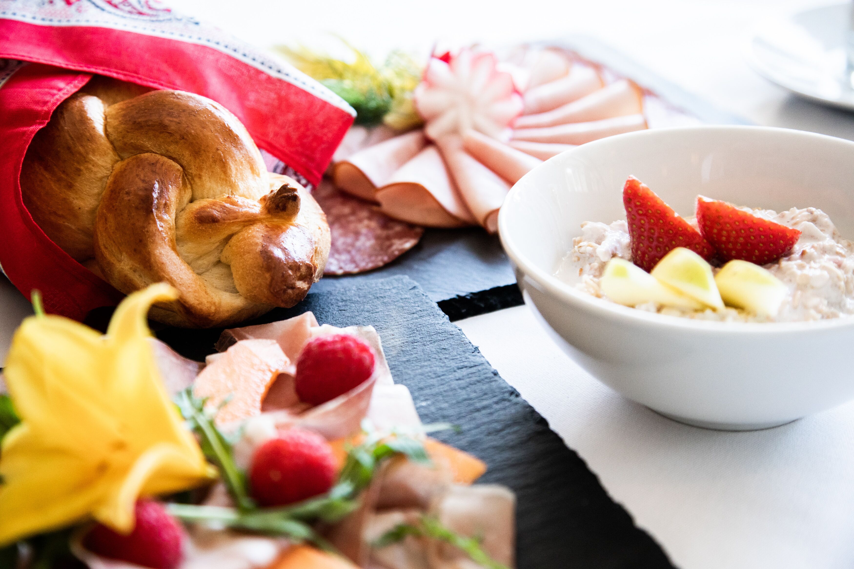 A table with a loaf of bread, a bowl of oatmeal with strawberries, and various pastries.