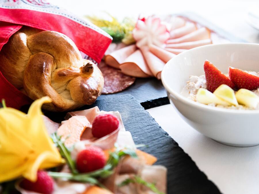 A table with a loaf of bread, a bowl of oatmeal with strawberries, and various pastries.