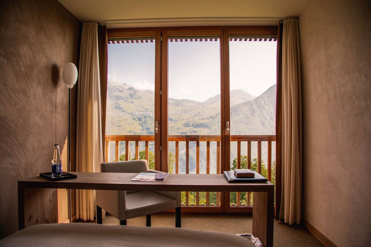 Ein Hotelzimmer mit großem Fenster, Schreibtisch, Stuhl und Bett.