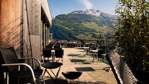 Terraza exterior con mesas y sillas, con vista a un paisaje montañoso.