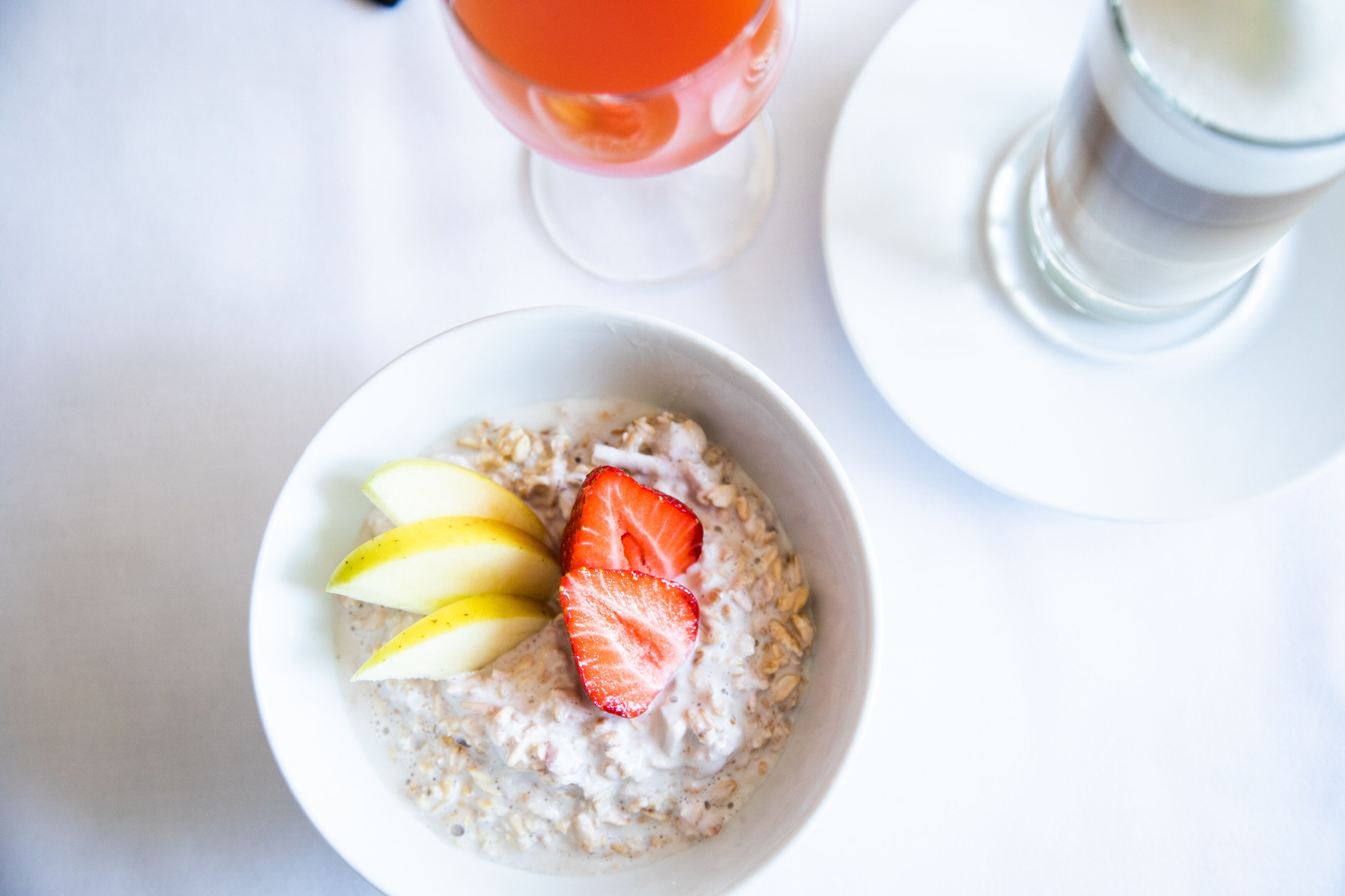 A bowl of oatmeal with sliced apples and a strawberry on a white plate.