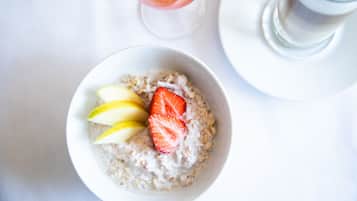Un tazón de avena con rodajas de manzana y una fresa sobre un plato blanco.