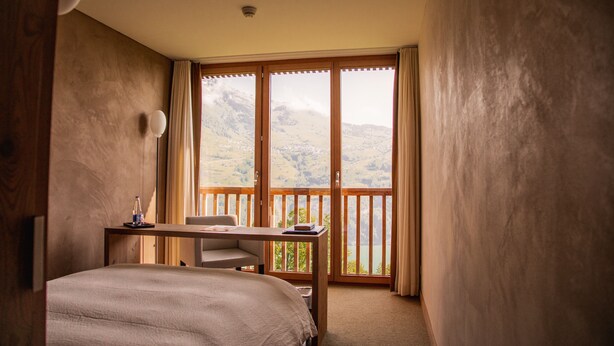 Un dormitorio con una cama grande, un escritorio y vistas a las montañas a través de una puerta corredera.