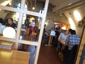 Vista interior de un restaurante con mesas y sillas de madera, paredes de piedra y un cartel de menú a la vista.