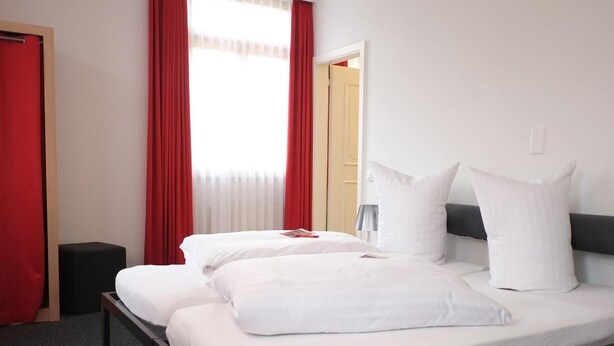A double bed with white bedding, a small bedside table, and a red curtain. - Hotel Brauerei Frohsinn (Arbon)