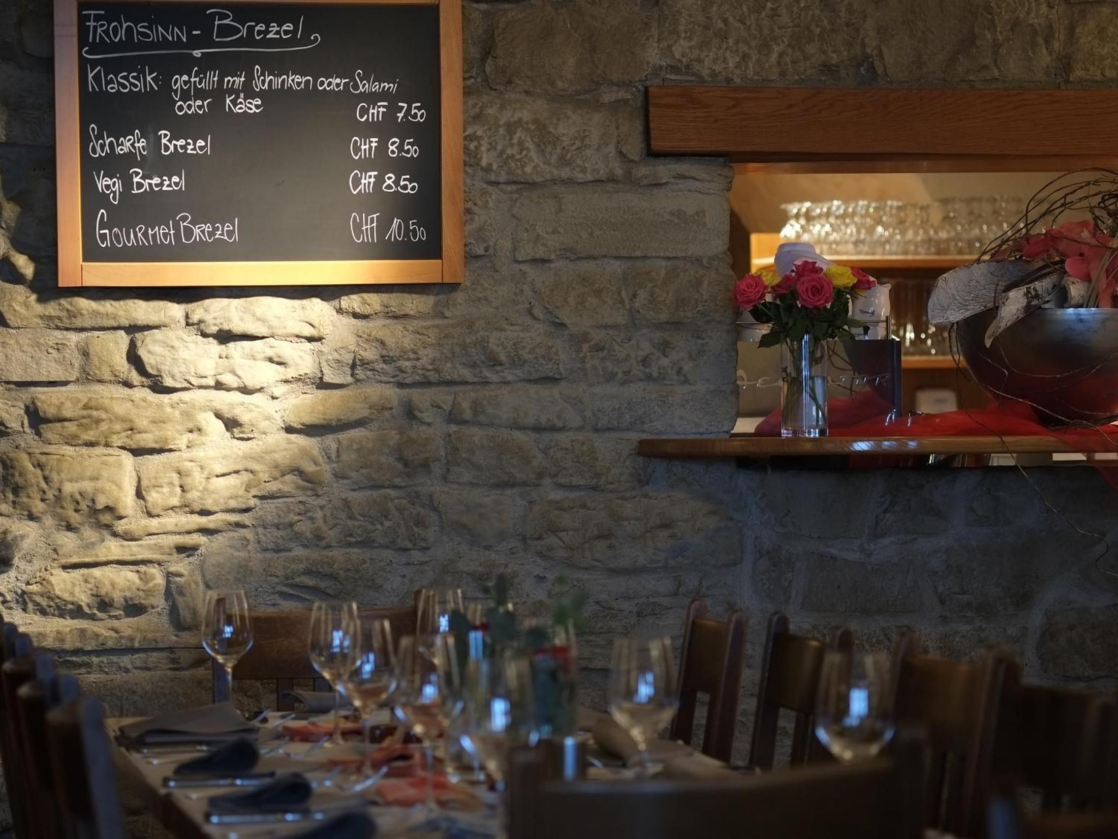 Interior de restaurante con una pizarra que muestra un menú con diferentes platillos de pretzel y sus precios.