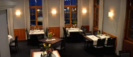 A hotel dining area with multiple tables, candles, and a view of the night sky through windows.